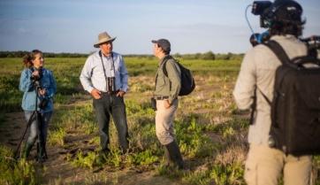 People in a field being recorded by a person with their back to the camera