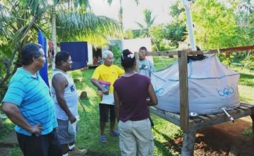 people listening to a person speaking next to a water tank