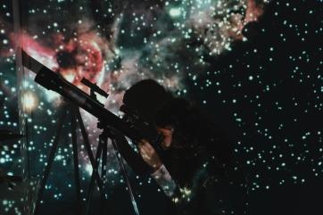 A young person looking through a telescope against a starry wall.